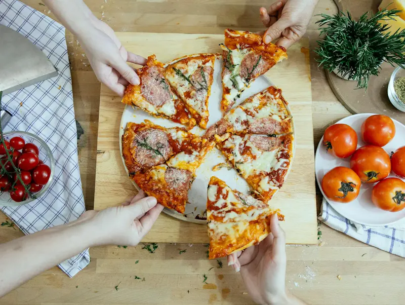 Fotografía de Benvenuti al sud Crop friends taking slices of delicious pizza from cutting board | Foto de Katerina Holmes, en https://www.pexels.com/@katerina-holmes?utm_source=centralapp&utm_medium=referral