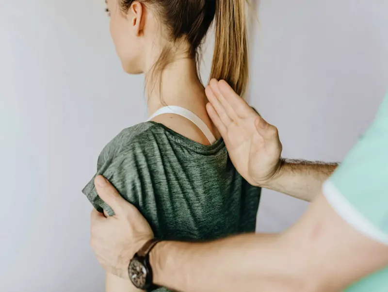 Back view of crop unrecognizable osteopath in uniform and wristwatch checking up back of slim female patient in casual wear on white background | Photo de Karolina Grabowska www.kaboompics.com, sur https://www.pexels.com/@karola-g?utm_source=centralapp&utm_medium=referral