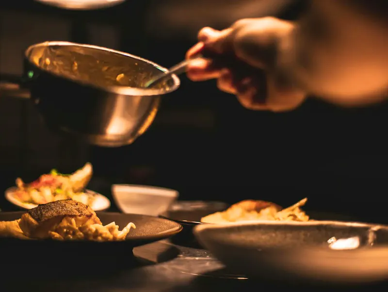 Gourmet dish being plated by a chef in a dimly lit restaurant's kitchen. | Photo by Yente Van Eynde, on https://www.pexels.com/@yente-van-eynde-1263034?utm_source=centralapp&utm_medium=referral