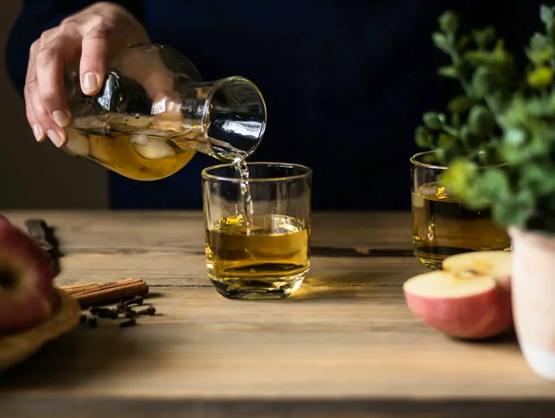 Close-up of someone pouring apple cider into glasses on a wooden table with apples and spices. | Immagine di Anna Pyshniuk, su https://www.pexels.com/@anna-pyshniuk-2453945?utm_source=centralapp&utm_medium=referral