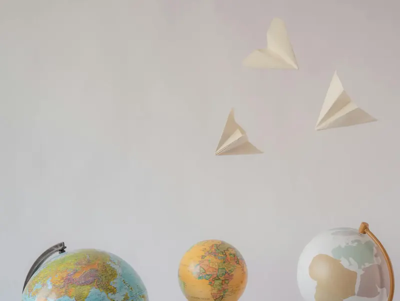 Paper airplanes fly over colorful globes, symbolizing travel and exploration on a white background. | Photo de Marina Leonova, sur https://www.pexels.com/@marina-zasorina?utm_source=centralapp&utm_medium=referral