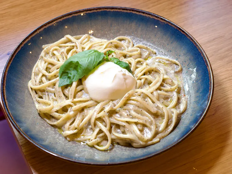 Découvrez les Linguine al Tartufo, la spécialité emblématique de Ti Amo. Ces pâtes fraîches sont nappées d'une crème de truffe onctueuse, agrémentées de parmesan et de mozzarella fondante. Le clou du spectacle ? Une burrata entière déposée sur le dessus, offrant un cœur ultra-crémeux pour les amateurs de cuisine italienne authentique.
