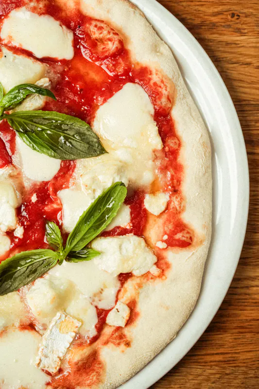 La pizza Margherita classique du restaurant Ti Amo : une pâte artisanale aux bords gonflés et croustillants, garnie d'une sauce tomate savoureuse, de mozzarella fondante et de feuilles de basilic frais.