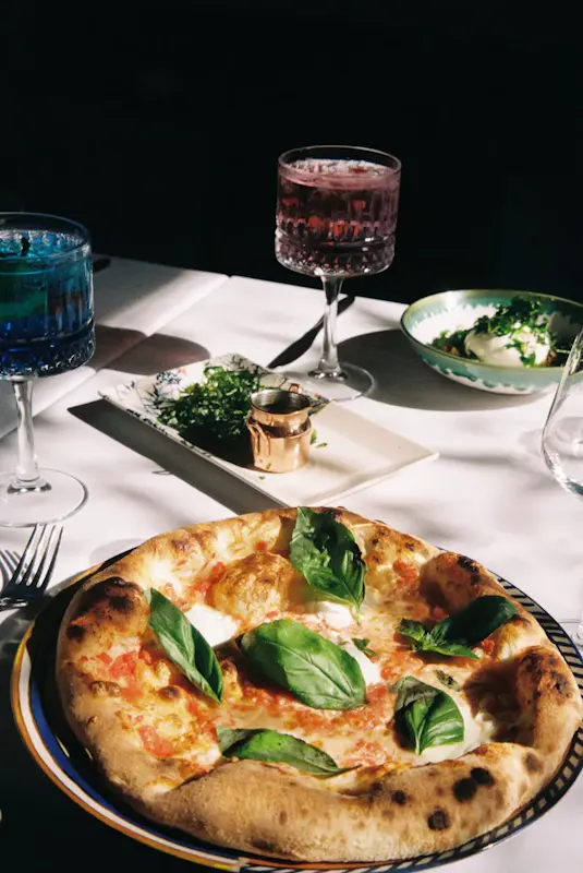 Fresh Italian pizza with basil on a table with drinks and side dishes. | Photo by Alexandra Stroescu, on https://www.pexels.com/@alexandra-stroescu-1044324559?utm_source=centralapp&utm_medium=referral