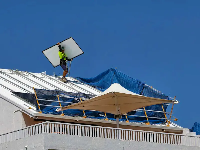 a man on top of a roof fixing a solar panel | Immagine di David Clode, su https://unsplash.com/@davidclode?utm_source=centralapp&utm_medium=referral